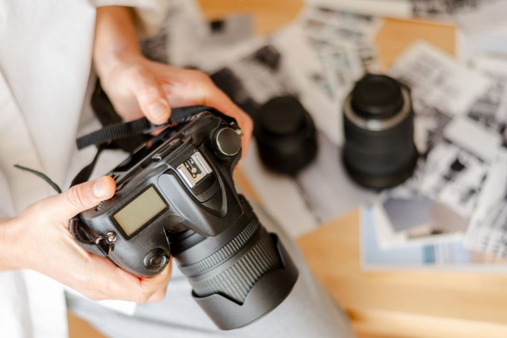 A photographer inspecting a used DSLR camera on a desk covered with prints, illustrating Why Verifying Sellers Changes the Game for Used Camera Buyers.