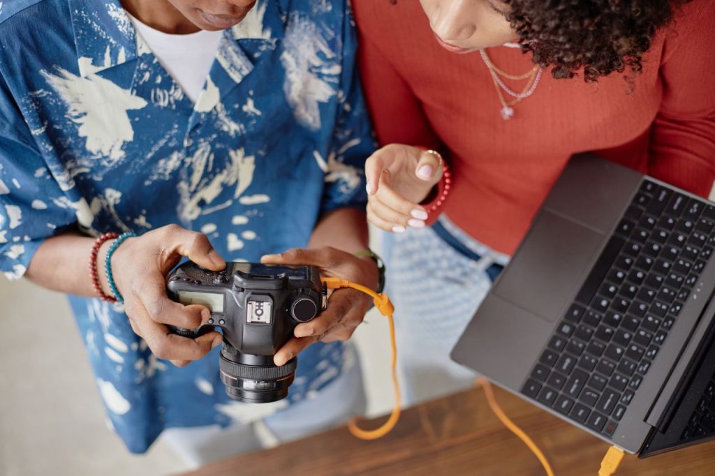 Two people reviewing a used DSLR camera while working beside a laptop, illustrating Why Verifying Sellers Changes the Game for Used Camera Buyers.