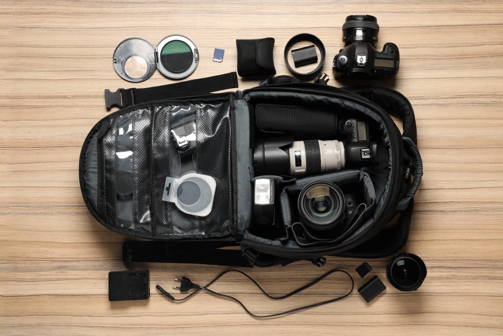 Camera bag laid open with mirrorless camera bodies, lenses, batteries, and accessories arranged on a wooden surface, representing the most exciting camera & lens releases to watch in 2026.