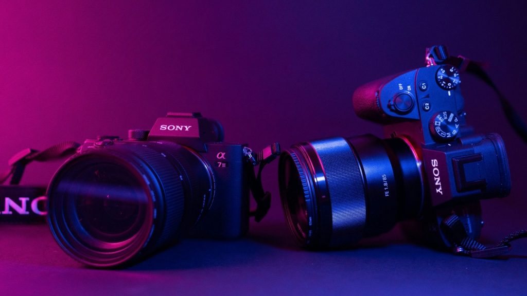 Two Sony mirrorless cameras under purple lighting representing different versions of a photographer’s Main Character Camera.