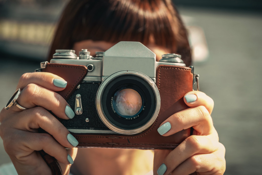 person holding a vintage film SLR camera with a leather half-case up to their face outdoors