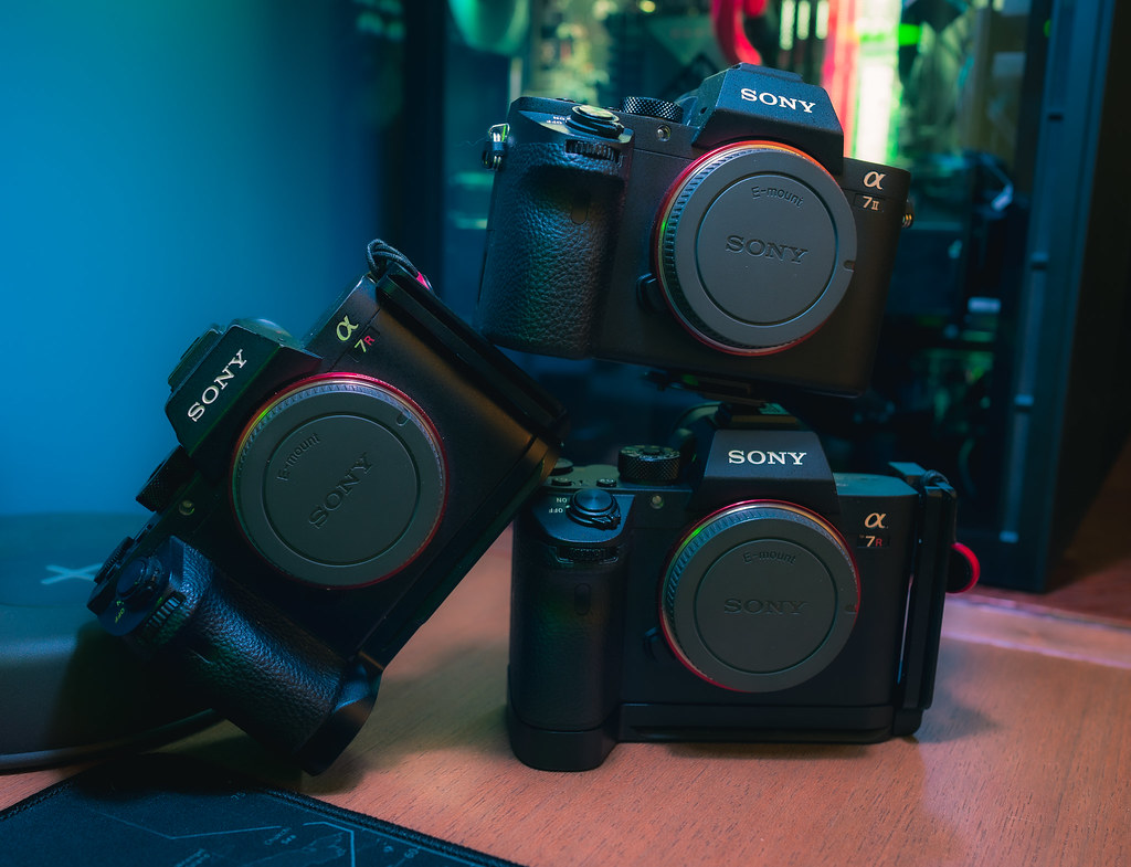 three Sony mirrorless camera bodies arranged on a wooden desk under colored lighting