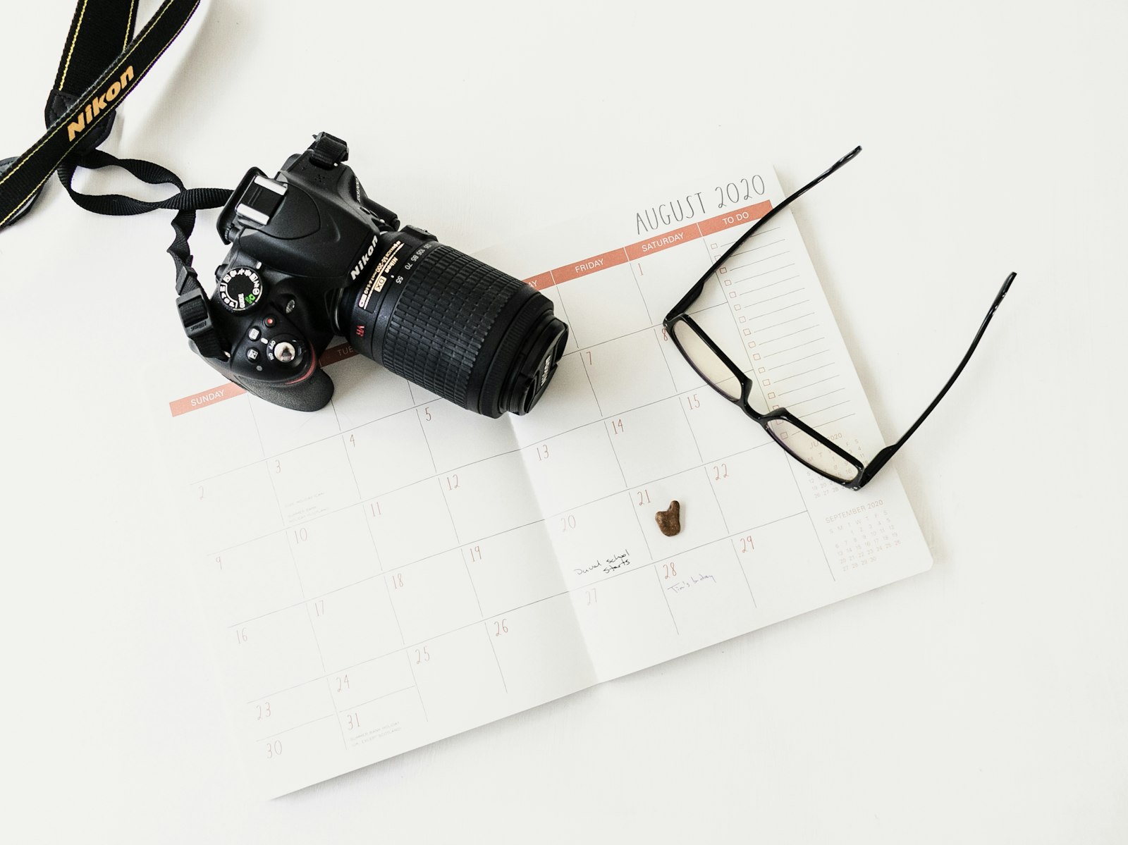 black Nikon DSLR camera resting on a calendar page next to eyeglasses