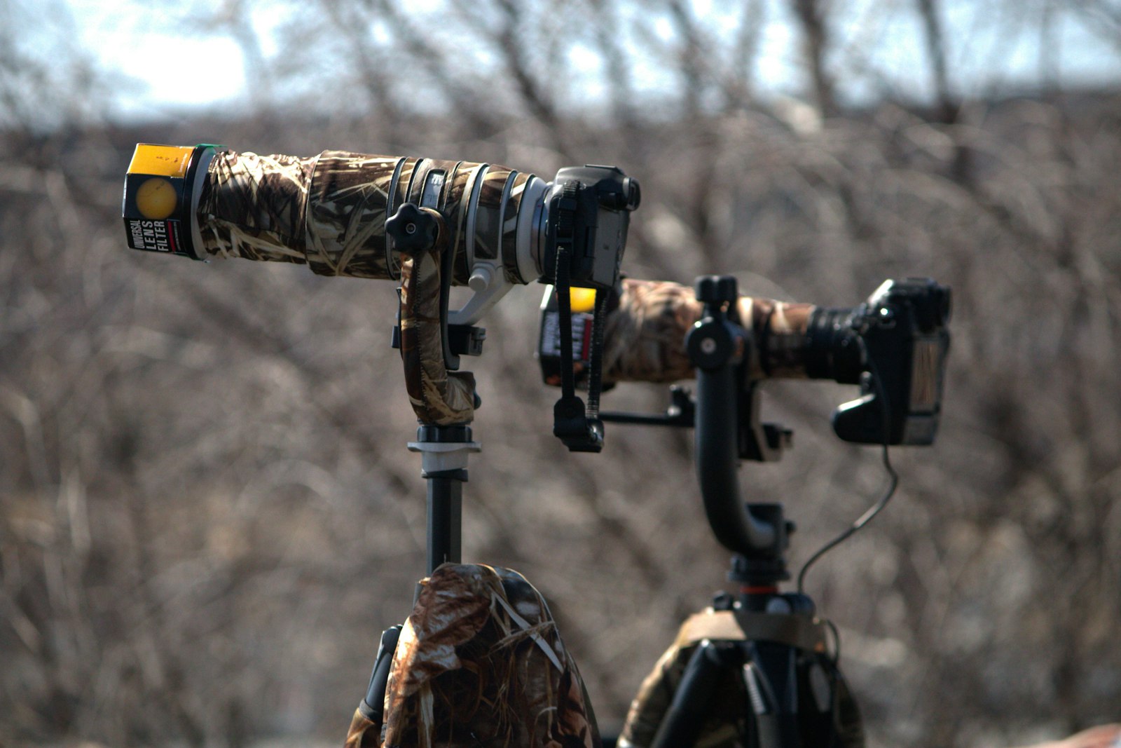 large camouflaged telephoto lens mounted on a tripod with gimbal head outdoors