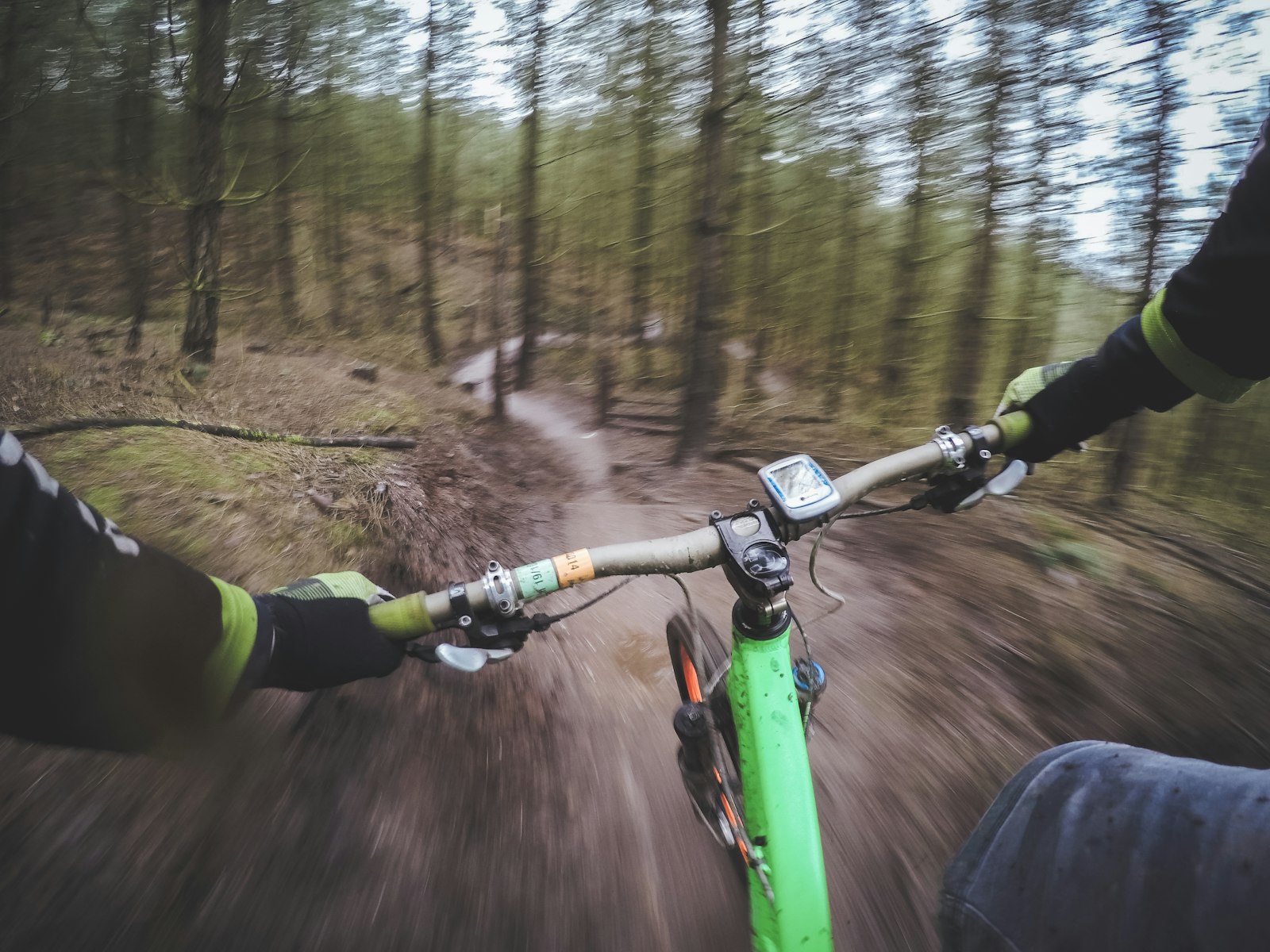 first-person view of hands gripping handlebars while riding a green mountain bike on a forest trail