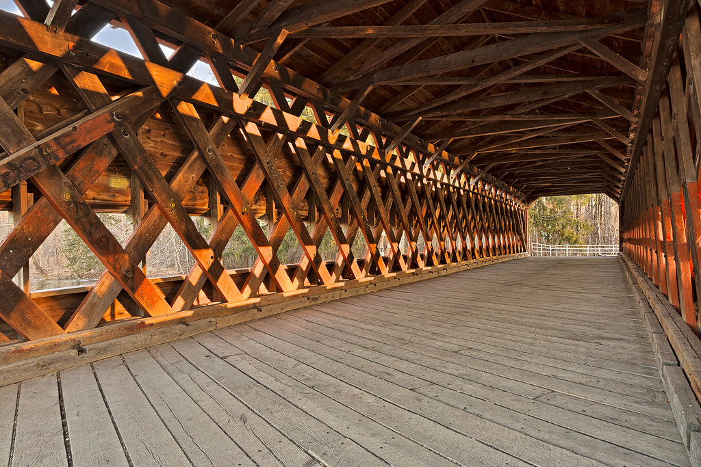 wide-angle interior view of a wooden covered bridge with crisscrossing lattice beams and plank flooring