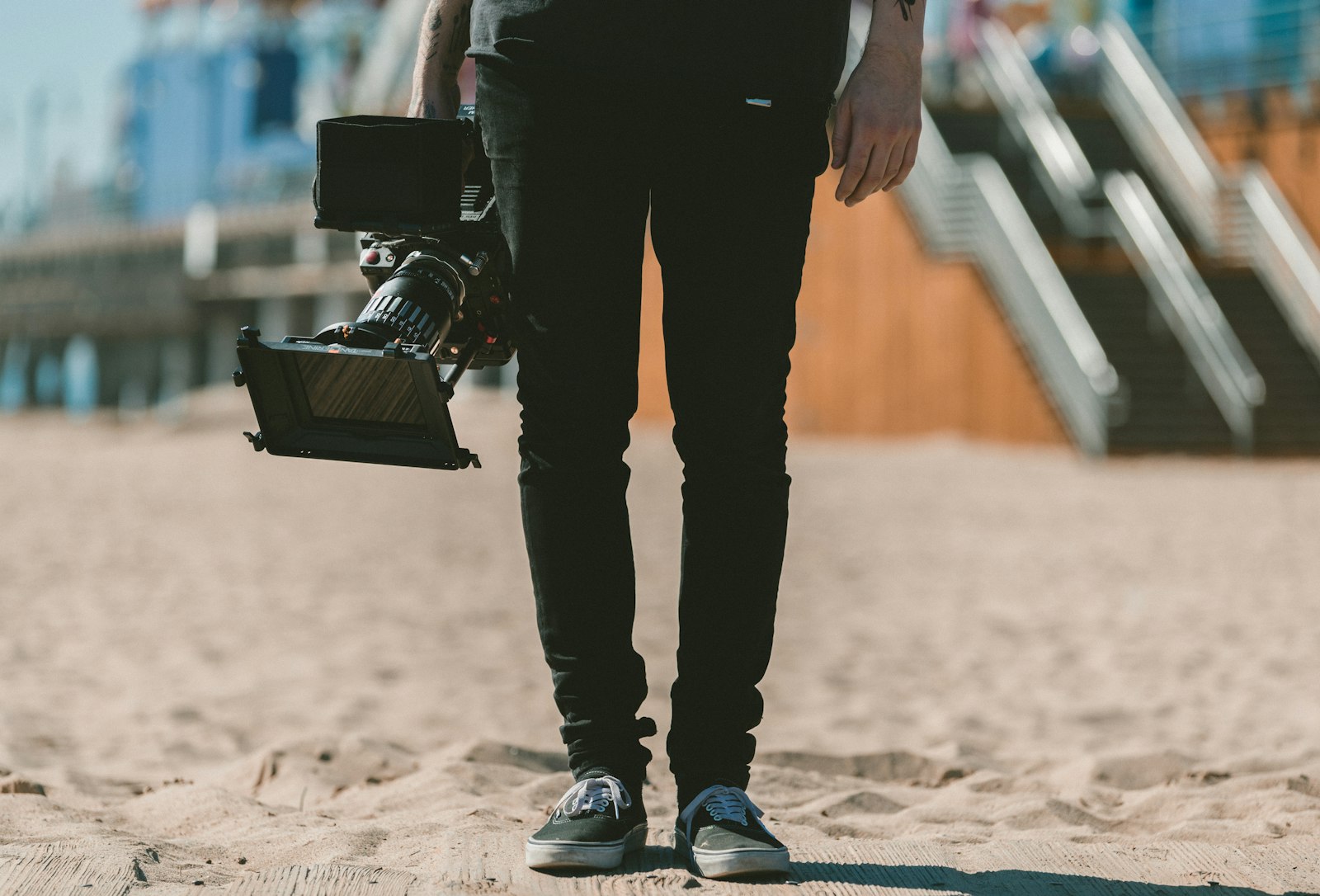 videographer walking on a beach holding a shoulder-mounted cinema camera rig in warm daylight