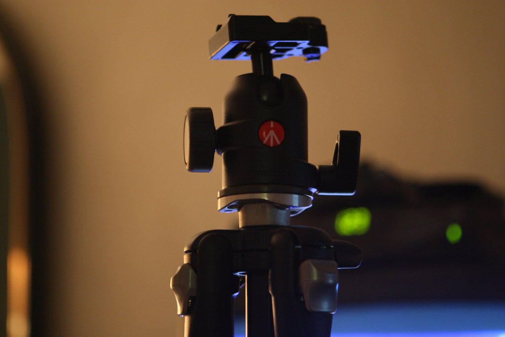 close-up of a black tripod head with locking knobs and leg lock levers against a warm-toned background