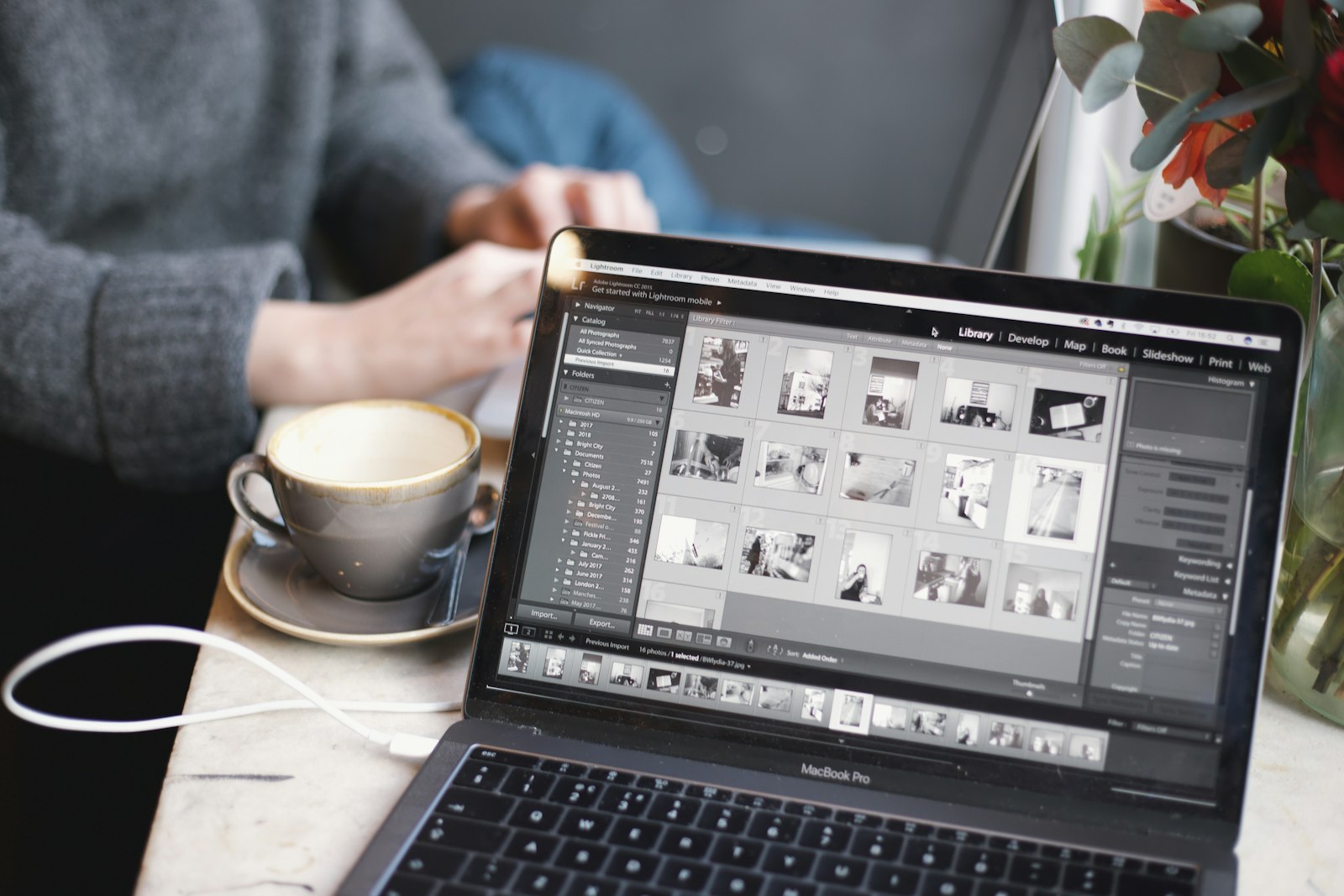 person reviewing photos in editing software on a laptop beside a coffee cup at a cafe table