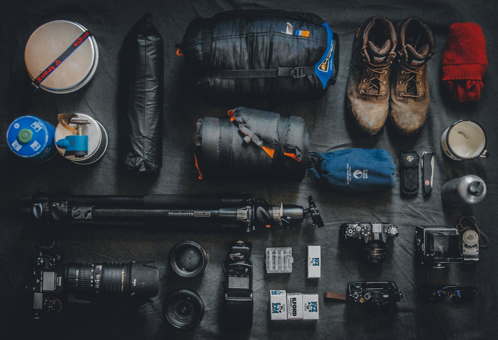 flat-lay of modern camera gear including a folded tripod, lenses, bags, and boots on a dark surface