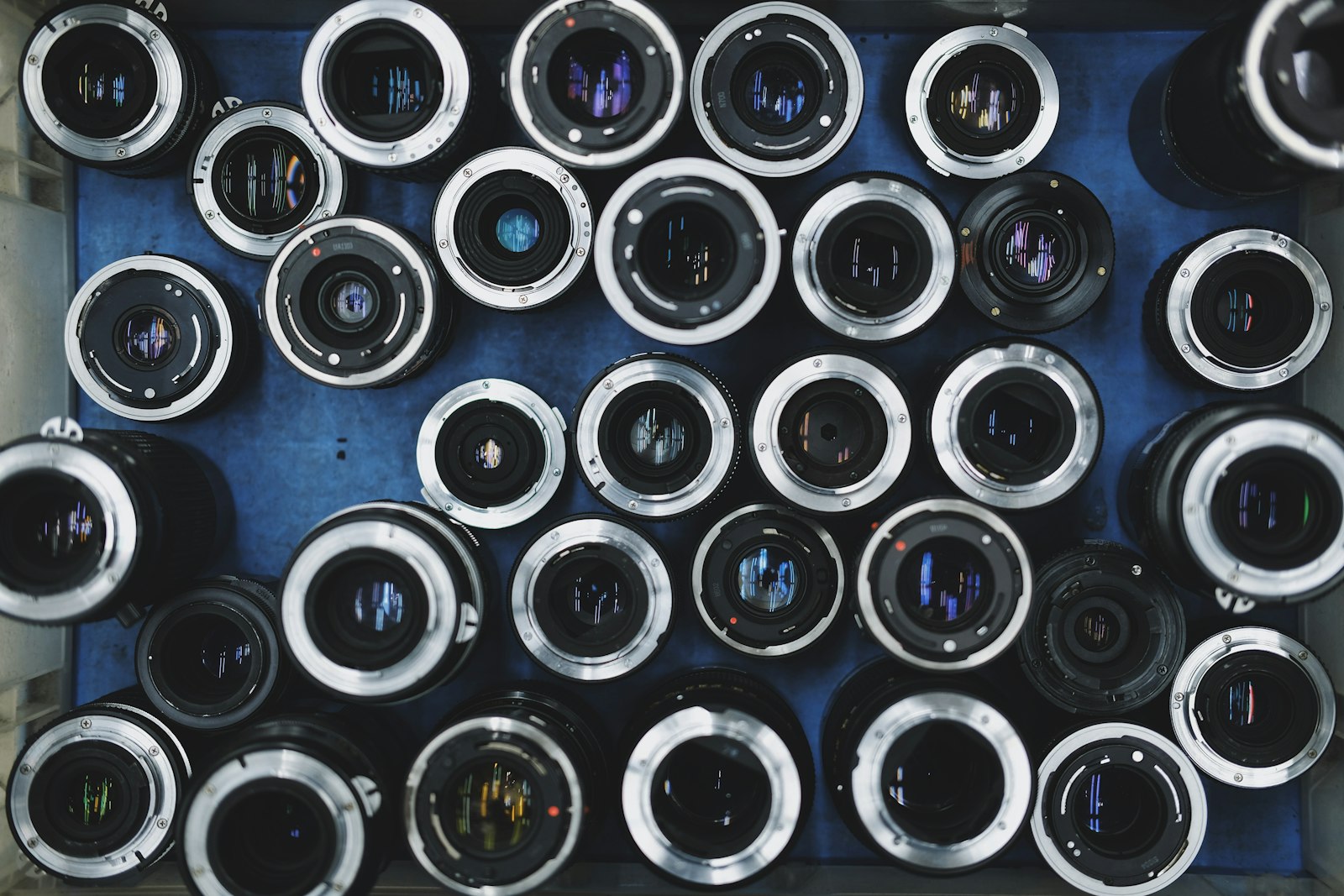 collection of vintage manual focus camera lenses arranged in a grid on a blue surface